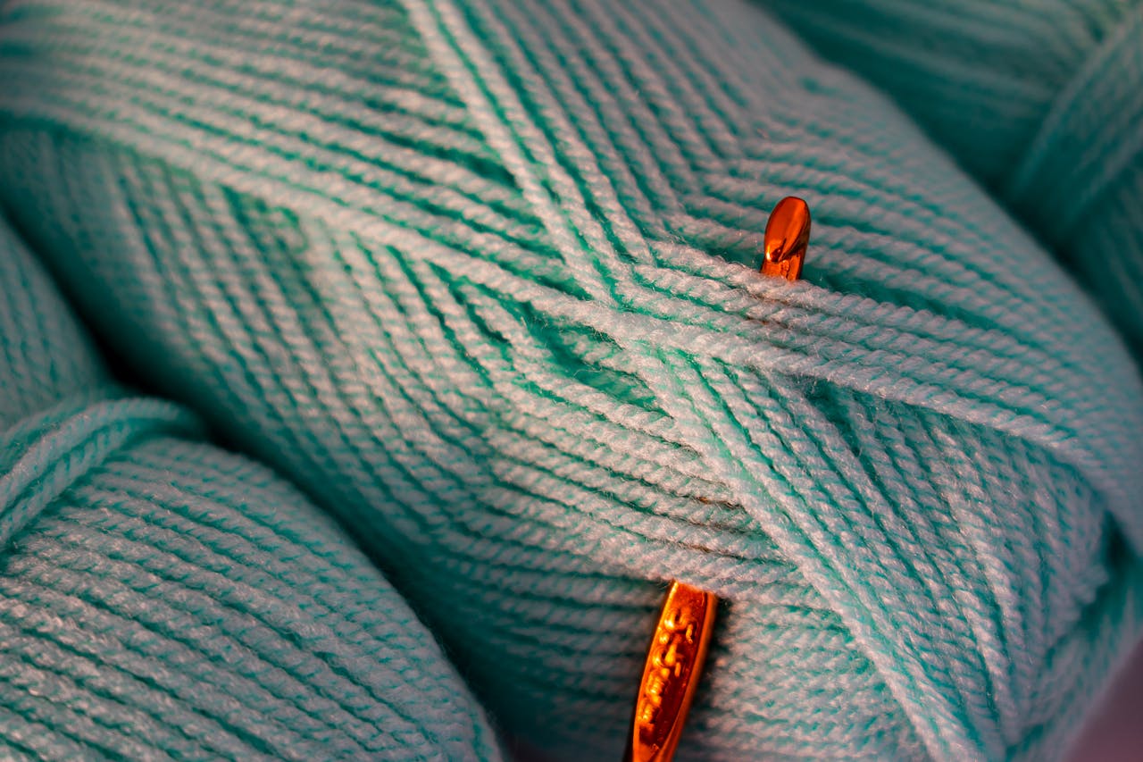 A detailed close-up of teal yarn intertwined with an orange crochet hook, highlighting texture.